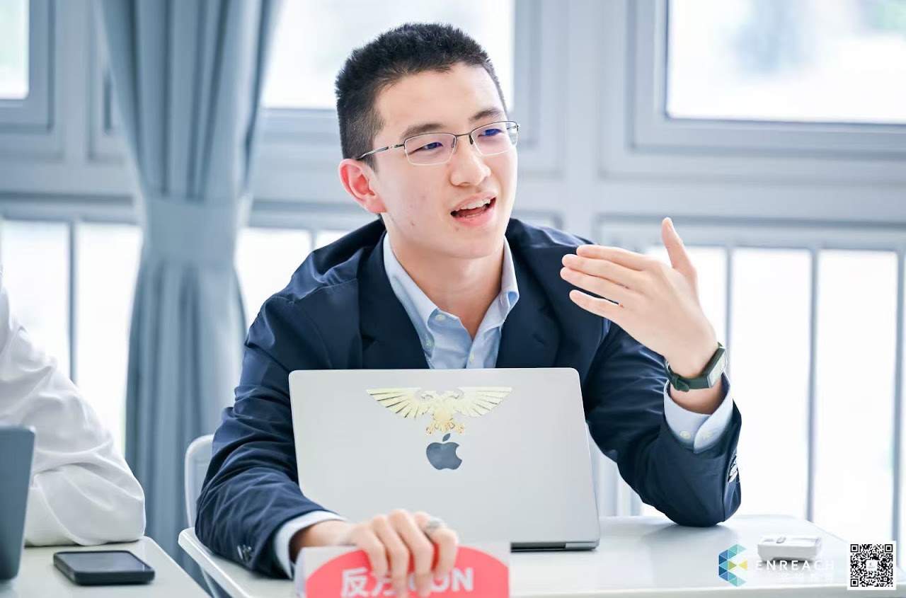 Chris Wan speaking and gesturing from behind a laptop during a public forum debate round